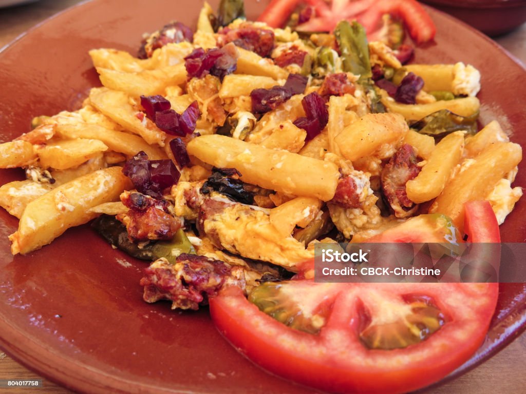 Spanish tapas dish of a scrambles of egg, peppers, tomatoes and chorizo and potato chips.